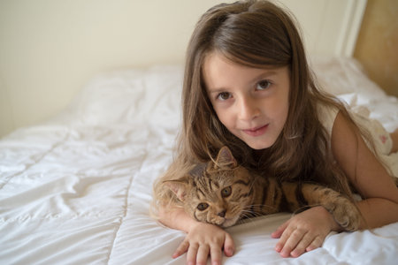 Young girl stroking cat lying on bedの写真素材