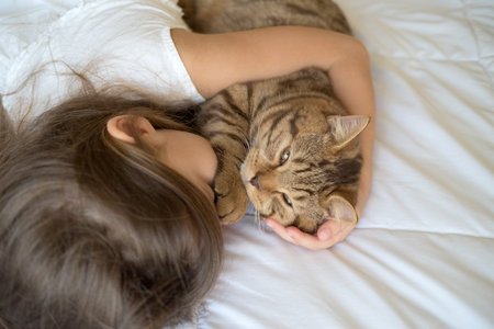 Young girl stroking cat lying on bedの写真素材