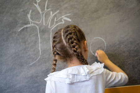 Rear view of little girl writing on blackboardの写真素材