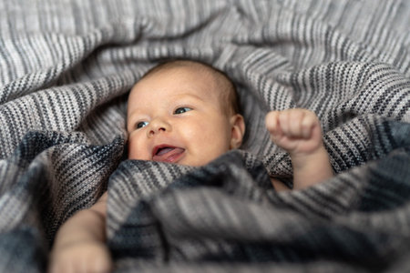Cute newborn baby girl, wrapped in blanket, lying in bed