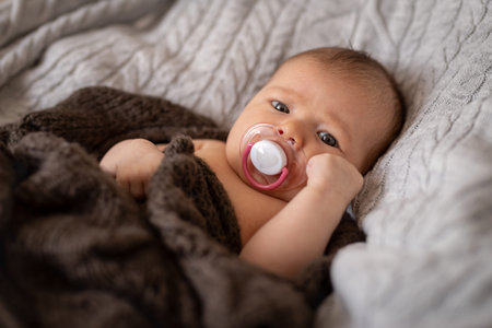 Cute baby girl with pacifier wrapped in blanket