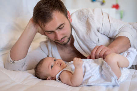 Father bonding with his baby girl, while both resting on the bedの写真素材