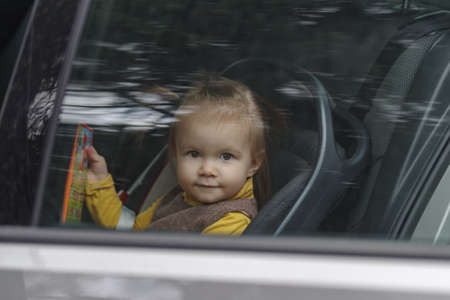 Cute and lovely toddler girl, sitting on a backseat, looking through a car windowの写真素材