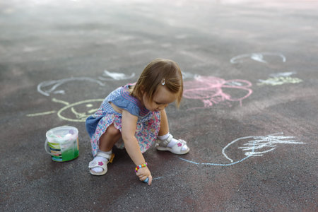 Overhead shot of a little girl scribbling in colorful chalk on pavement