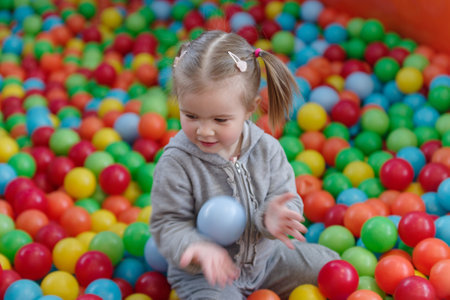 A little blond girl play in a ball pool full of multi colored ballの写真素材