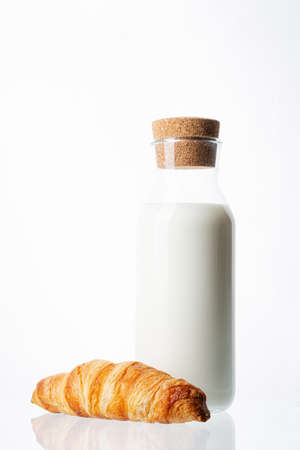 Bottle with milk on a white background. Glass bottle. Natural cork. White drink. Cow's milk. One classic french croissant on a white background. Homemade baking.の写真素材