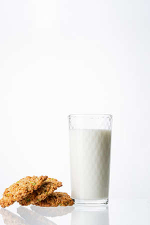 A glass filled with milk on a white background. White drink. Cow's milk. Homemade cookies on a white background. Pyramid of cookies. Cookies on top of each other.の写真素材