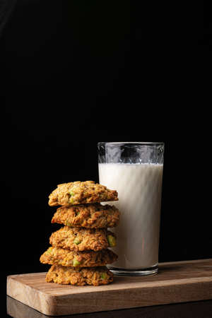 Glass with milk on a wooden board. Homemade cookies. Black background. White drink. Cow's milk. Pyramid of cookies. Cookies on top of each other.の写真素材