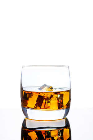 Glass of whiskey with ice on a white background. White background. Whiskey / Brandy / Cognac / Rum. Glass with a strong drink.の写真素材