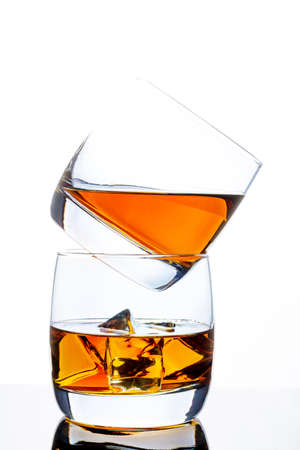 Two glasses of whiskey with ice. A pyramid of glasses. White background. Whiskey / Brandy / Cognac / Rum. Glass with a strong drink.の写真素材