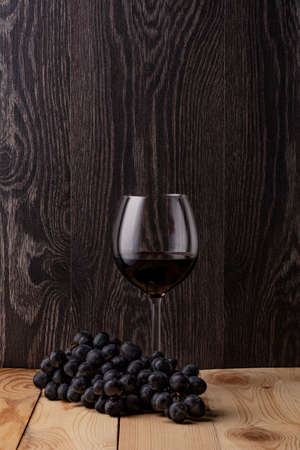 Wine bottle and a glass of wine. A bunch of ripe black grapes. Wooden background.の写真素材