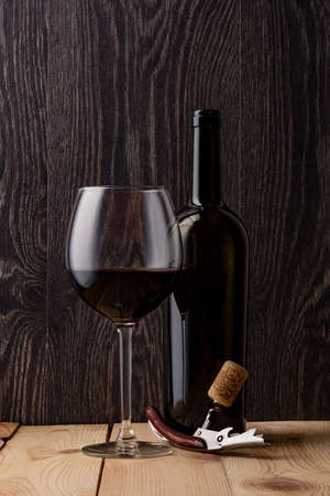Wine bottle and a glass of wine. Wood background. Natural cork. Metal corkscrew.の写真素材