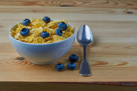 Cornflakes with milk for breakfast. Blueberries. Metal spoon. Wood background.の写真素材