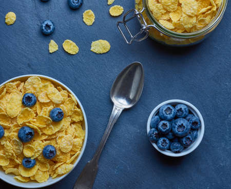Cornflakes with milk for breakfast. Blueberries. Metal spoon. Background with stone texture. View from above. Flat lay.の写真素材