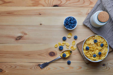 Cornflakes with milk for breakfast. Blueberries. Milk in a glass bottle. Metal spoon. Linen napkin. Wood background. View from above. Flat lay.の写真素材
