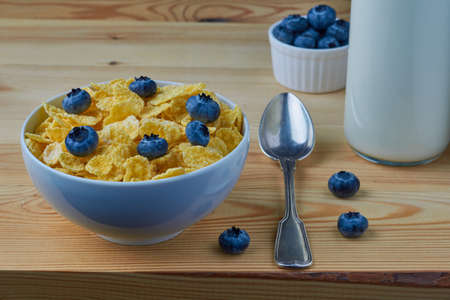 Cornflakes with milk for breakfast. Blueberries. Milk in a glass bottle. Metal spoon. Wood background.の写真素材