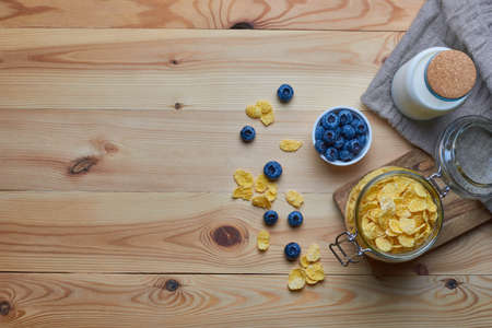 Cornflakes with milk for breakfast. Blueberries. Milk in a glass bottle. Linen napkin. Wood background. View from above. Flat lay.の写真素材