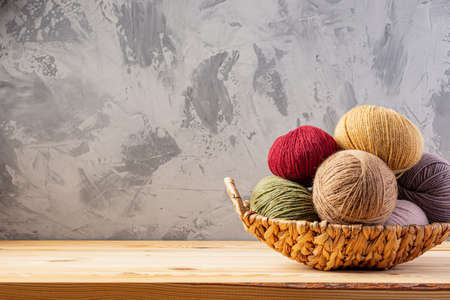 Skeins of yarn for knitting from natural wool in a wicker basket. Wooden surface or table. Background - concrete wall.の写真素材