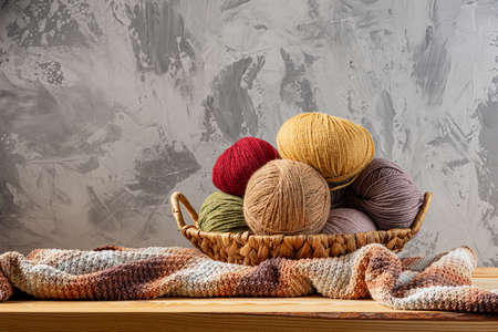 Skeins of yarn for knitting from natural wool in a wicker basket. Wooden surface or table. Background - concrete wall. Wooden knitting needles.の写真素材