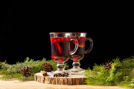 Two glasses with homemade mulled wine on a wooden saw. Black background. Real spruce branches. Fir cones.の写真素材