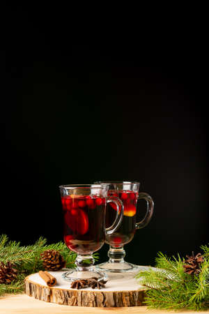 Two glasses with homemade mulled wine on a wooden saw. Black background. Real spruce branches. Fir cones.の写真素材
