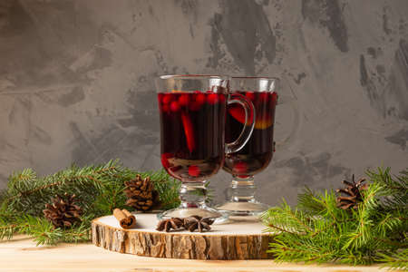 Two glasses with homemade mulled wine on a wooden saw. Concrete background. Real spruce branches. Fir cones.の写真素材