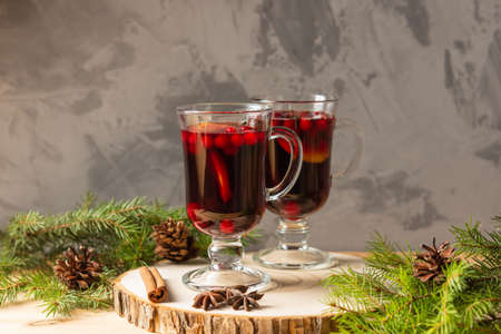 Two glasses with homemade mulled wine on a wooden saw. Concrete background. Real spruce branches. Fir cones.の写真素材