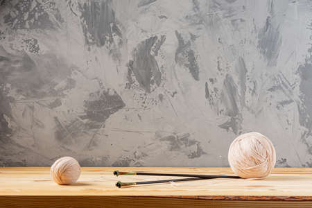 Skeins of yarn for knitting from natural wool on a wooden surface or table. Background - concrete wall. Wooden knitting needles.の写真素材