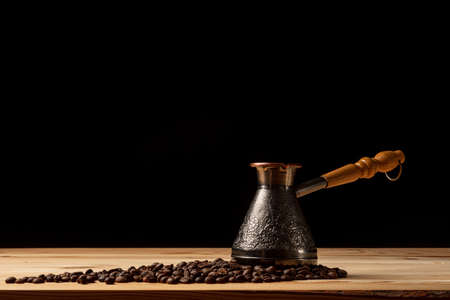 Copper cezve with coffee on the table. Freshly brewed coffee. Countertop made of wood. Coffee beans. Freshly fried arabica. Black background.の写真素材