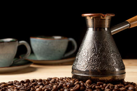 Copper cezve with coffee on the table. Freshly brewed coffee. Countertop made of wood. Coffee beans. Freshly fried arabica. Black background.の写真素材