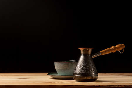 Copper cezve with coffee on the table. Freshly brewed coffee. Countertop made of wood. Coffee beans. Freshly fried arabica. Black background.の写真素材