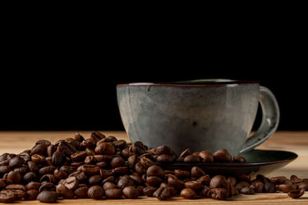 Handmade cup with coffee on the table. Countertop made of wood. Coffee beans. Black background.の写真素材