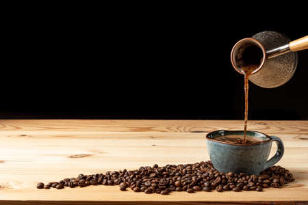 Handmade cup with coffee on the table. Countertop made of wood. Coffee beans. Black background.の写真素材