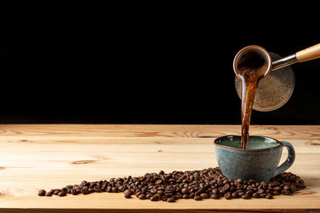 Handmade cup with coffee on the table. Countertop made of wood. Coffee beans. Black background.の写真素材