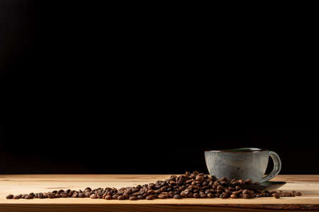 Handmade cup with coffee on the table. Countertop made of wood. Coffee beans. Black background.の写真素材