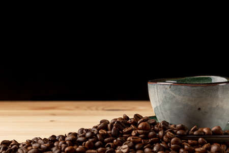Handmade cup with coffee on the table. Countertop made of wood. Coffee beans. Black background.の写真素材
