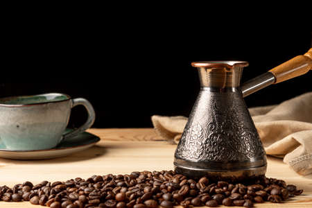 Copper cezve with coffee on the table. Freshly brewed coffee. Countertop made of wood. Coffee beans. Freshly fried arabica. Black background.の写真素材