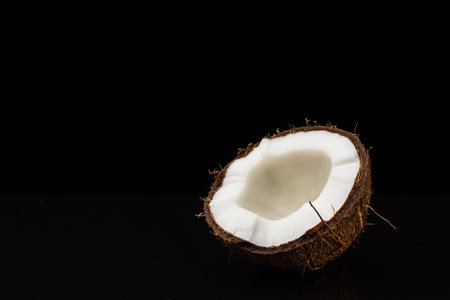 Coconut on a black background. One halve of a nut. Coconut chopped in half. White flesh.