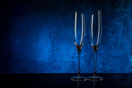 Two glasses for champagne on a black mirror surface. Blue background Concrete wall. Black glass. Crystal glassの写真素材
