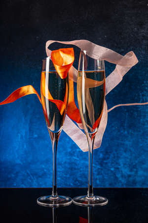 Two glasses with champagne on a black mirror surface. Flying satin ribbon. Blue background Concrete wall. Black glass. Crystal glassの写真素材