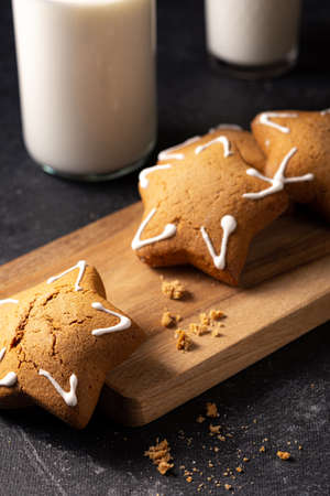 Handmade custard gingerbread in the shape of a star on a black background. Homemade baking. A bottle of milk in the background. Wooden plank. Baking crumbs.の写真素材