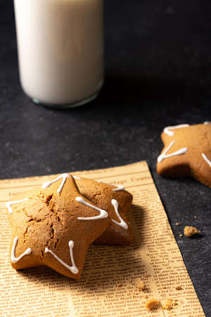 Handmade custard gingerbread in the shape of a star on a black background. Homemade baking. A bottle of milk in the background. Old newspaper. Baking crumbs.の写真素材