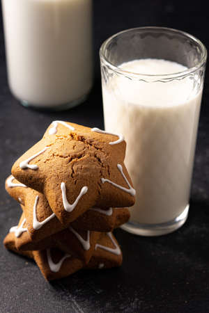 Handmade custard gingerbread in the shape of a star on a black background. Homemade baking. A bottle of milk in the background. Board made of stone.の写真素材