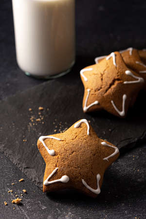 Handmade custard gingerbread in the shape of a star on a black background. Homemade baking. A bottle of milk in the background. Board made of stone. Baking crumbs.の写真素材