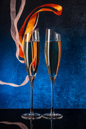 Two glasses with champagne on a black mirror surface. Flying satin ribbon. Blue background Concrete wall. Black glass. Crystal glassの写真素材