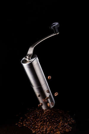 Manual coffee grinder on a black background. Metal coffee grinder. Flying coffee beans. A scattering of coffee beans on a dark background.の写真素材