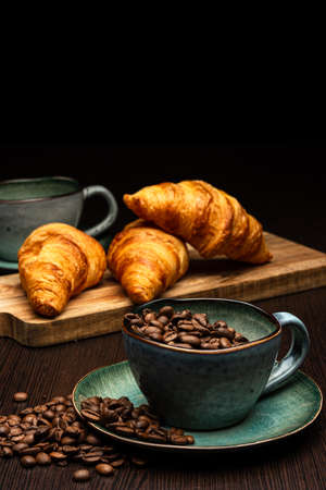 Cup with coffee beans on a black background. Freshly roasted arabica. Several fresh croissants on a wooden board.の写真素材