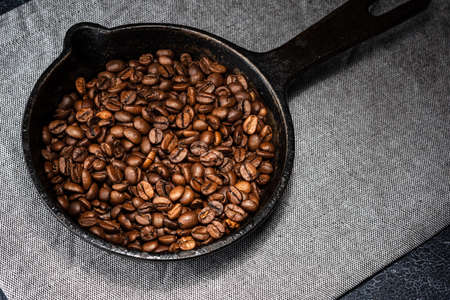 Freshly roasted coffee beans in a cast iron skillet. Linen napkin. A natural stone. Dark background.の写真素材