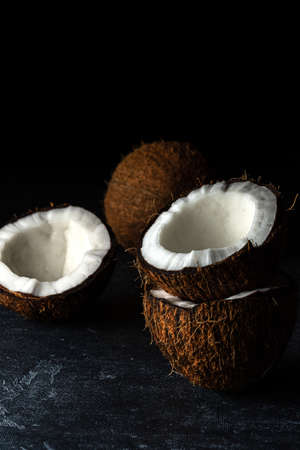 Coconut on a black background. Chopped coconut. Several parts. Stone surface. Fresh coconut. White pulp.の写真素材