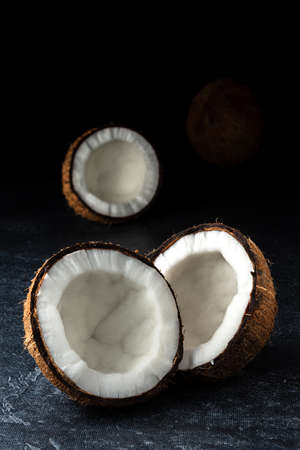 Coconut on a black background. Chopped coconut. Several parts. Stone surface. Fresh coconut. White pulp.の写真素材